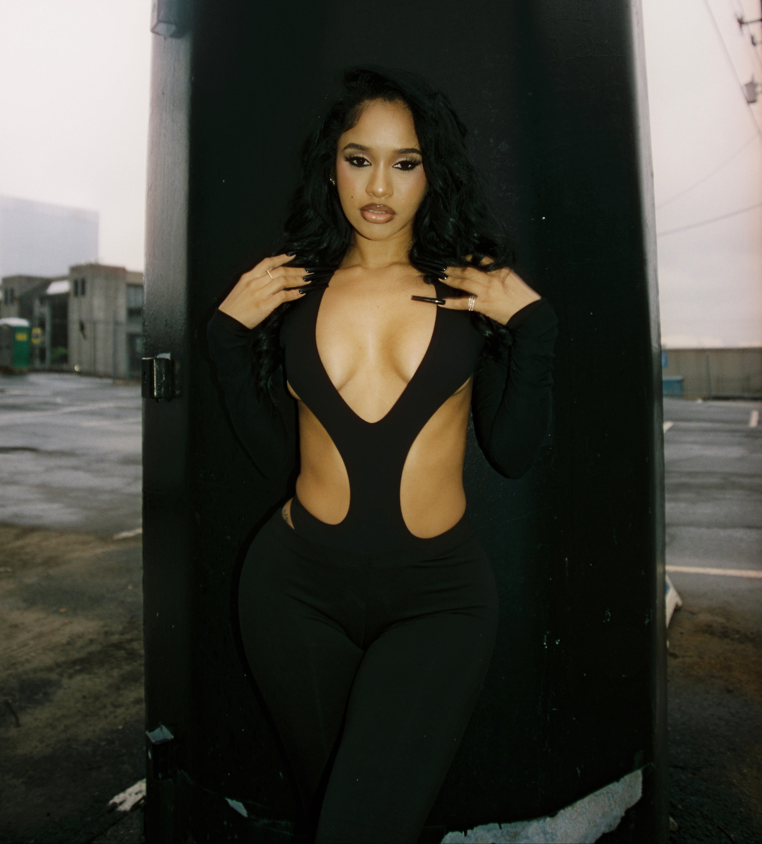 Woman wearing a black bodysuit with cut-out design against a dark background